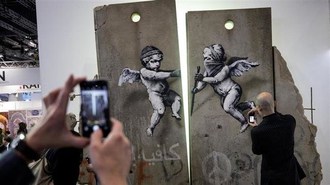 Visitors take photographs of the 'replica separation barrier' created by British street artist Banksy as it stands on display at the Palestine tourist stand at the World Travel Market at the Excel centre in London. (Photo by Reuters)