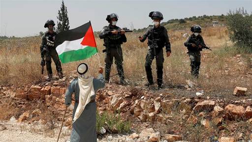 A demonstrator holds a Palestinian flag in front of Israeli forces during a protest against Israel's plan to annex parts of the illegally occupied West Bank, near Tulkarem [File: Mohamad Torokman/Reuters]
